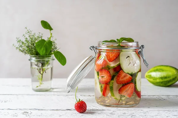 Infused water in glass jar with strawberry and a meloncella that is hybrid of cucumber and melon, thyme, Copy space. Healthy beverage concept without sugar added