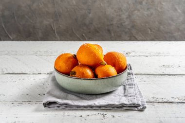 Kasede su damlası olan Medlar meyveleri, beyaz ahşap ve beton arka planda tabağın altında gri peçeteler. Merkezi bileşim.