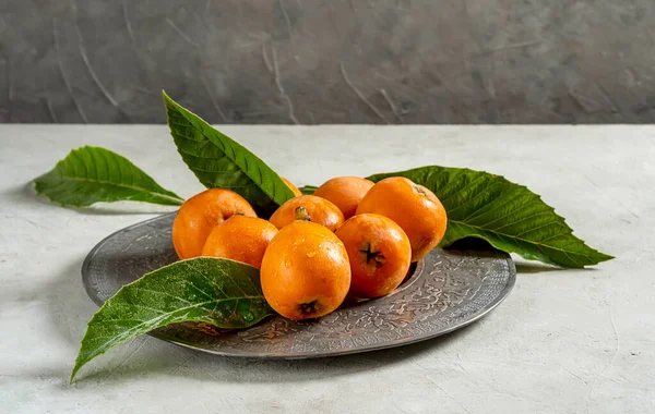 Medlar fruits on antique tin plate with fresh leaves over concrete background.