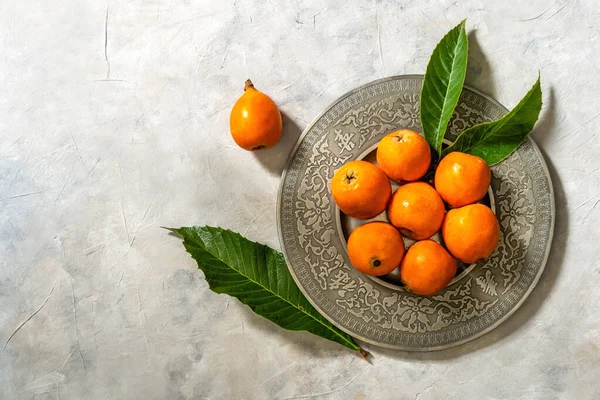 Medlar fruits on antique tin plate with fresh leaves over concrete background. Flat lay. Copy space
