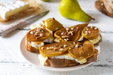 Camembert peyniri ve fındıklı karamelize armut ve tam tahıllı ekmeğin üzerine bal. Beyaz ahşap arkaplan, kapat, seçici odak.