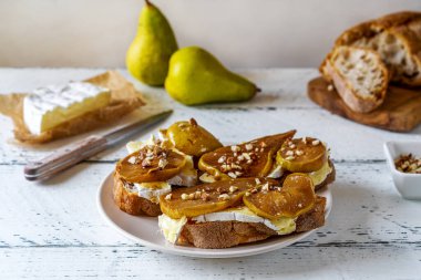 Camembert peyniri ve fındıklı karamelize armut ve tam tahıllı ekmeğin üzerine bal. Beyaz ahşap arka plan. Seçici odaklanma. Merkezi bileşim.