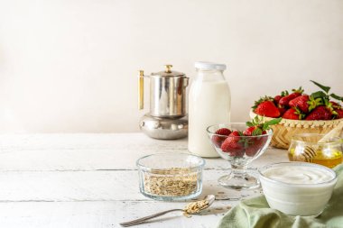 Çilekli kahvaltı konsepti, yoğurt, müsli, kahve demliği, sütlü şişe, bal. Beyaz ahşap arka plan. Uzayı kopyala Yatay yönelim. 