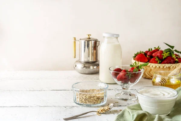 Çilekli kahvaltı konsepti, yoğurt, müsli, kahve demliği, sütlü şişe, bal. Beyaz ahşap arka plan. Uzayı kopyala Yatay yönelim. 