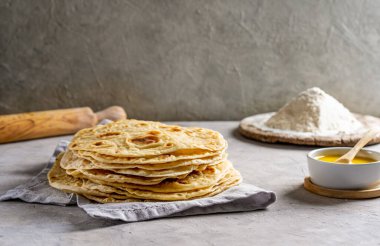 Ev yapımı Hint ekmeği Chapati ya da Roti gri beton arka planda gri peçeteyle tereyağlı ghee, merdane ve un. Geleneksel Asya yemeği. Seçici odak