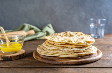 Ev yapımı Hint ekmeği Chapati veya Roti ahşap arka planda tereyağlı ghee, su, merdane ve yeşil peçeteli. Geleneksel Asya yassı ekmeği 