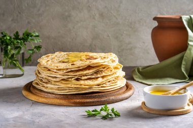 Ev yapımı Hint ekmeği Chapati veya Roti tereyağı ve kişniş ile gri beton arka planda. Çamur tenceresi, yeşil peçete arkası. Geleneksel Asya yemeği.
