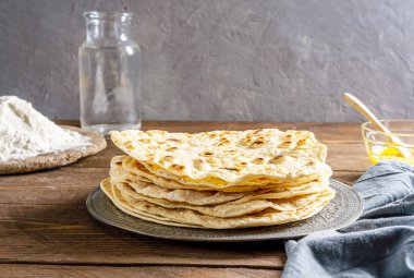 Ev yapımı Hint ekmeği Chapati veya Roti tereyağlı ghee, un, su ve gri peçeteli gri beton arka planda. Temel malzemeli geleneksel Asya düz ekmeği.