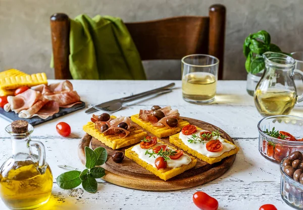Üzerine strakino peyniri, domates, otlar, benek ve zeytin konmuş ızgara polenta sosu. Beyaz ahşap arka plan. Arkada peçete olan sandalye..