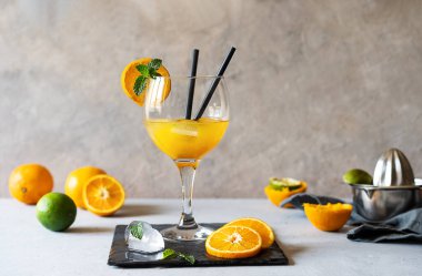 Sarı kuş kokteyli, rom, portakal ve limon suyu bardakta, iki pipet ve bir dilim portakal. Meyve, meyve sıkacağı, buz küpleri, beton zeminde taş tahta. Boşluğu kopyala