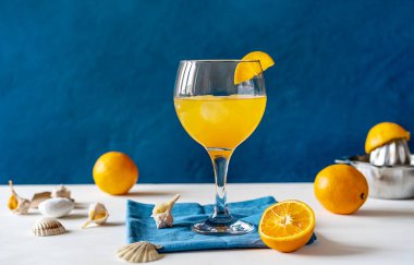 Sarı kuş kokteyli, rom, portakal ve limon suyu bardakta, bir dilim portakal, meyve suyu, meyve sıkacağı, beyaz masa kabukları, peçete. Mavi arka plan. Akdeniz ve deniz tarzı. Boşluğu kopyala