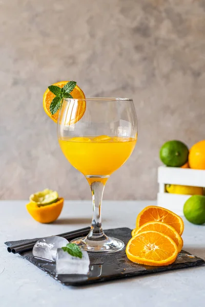 Yellow bird cocktail made with rum, ice, orange and lime juice in glass. Fruits, ice cubes, stone board on concrete background. Vertical banner. Copy space