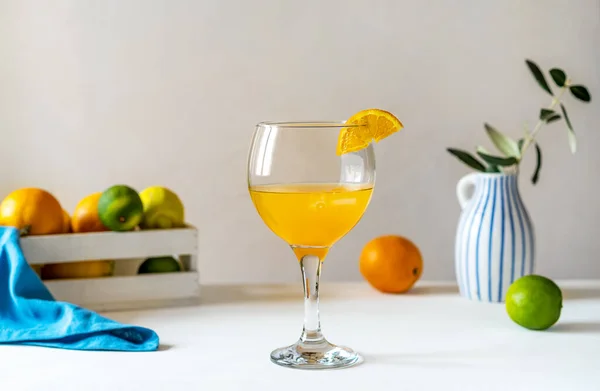 Yellow bird cocktail with rum, orange and lime juice with fruits on white background, blue napkin, wooden box with citrus fruits and vase with olive branch in the back. Mediterranean style. Copy space