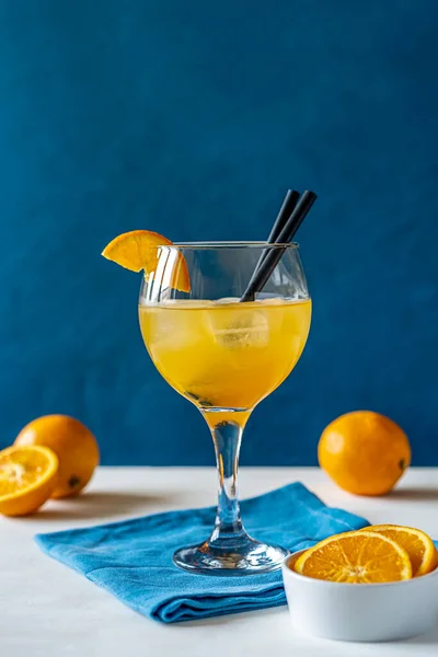 Yellow bird cocktail with rum, orange and lime juice in glass, fruits, blue napkin on white table. Dark blue background. Mediterranean or marine style. Vertical banner with copy space
