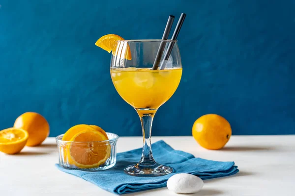 Yellow bird cocktail with rum, orange and lime juice in glass with straw, fruits on white table, blue napkin, blue or turquoise background. Mediterranean and marine style. Copy space