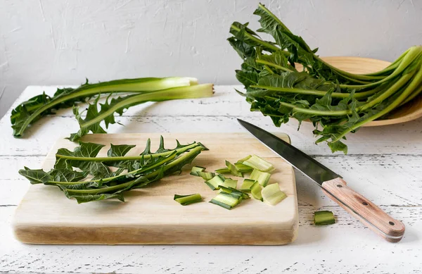 Chicory greens are low-calorie leafy vegetables, fount of inulin, vitamins and minerals. Healthy food concept. Cut leaves on cutting board with knife.