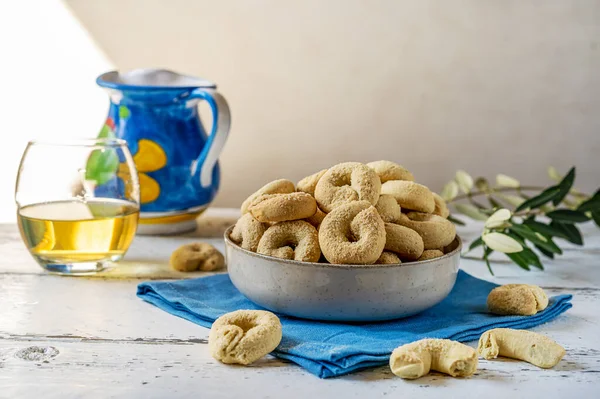 Sweet Italian cookies Taralli made with white wine, sugar, olive oil, eggs and flour. Cookies in bowl. blue napkin, wine decanter, olive brunch, glass of wine