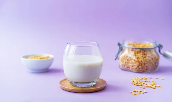 Vegan healthy pea milk in glass, pea seeds. Lilac background. Copy space. Healthy food concept. Selective focus