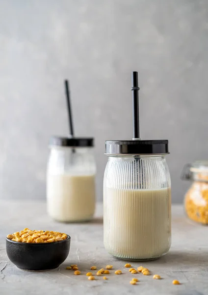 Vegan healthy plant pea milk in jars with drinking straws, yellow pea seeds, napkin and copy space. Concrete background. Vertical banner