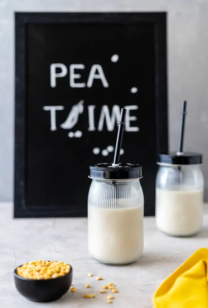 Vegan healthy plant pea milk in jars with drinking straws, yellow pea grains, napkin and mockup place. Concrete background. Vertical banner. Mockup