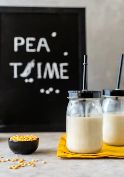 Vegan healthy plant pea milk in jars with drinking straws, yellow pea grains, napkin and mockup place. Concrete background. Vertical banner. Mockup