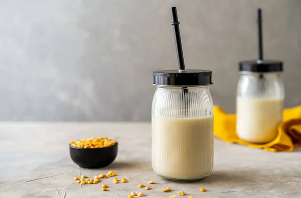 Vegan healthy plant pea milk in jars with drinking straws, yellow pea seeds, napkin and copy space. Concrete background.