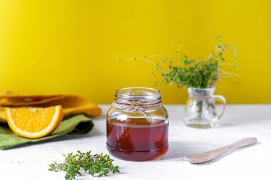 Küçük kavanozda sağlıklı turuncu kekik balı, taze kekik, portakal dilimleri, sarı arka planlı beyaz masa peçeteleri. Kekik balının antiseptik ve antibakteriyel faydaları vardır. Boşluğu kopyala