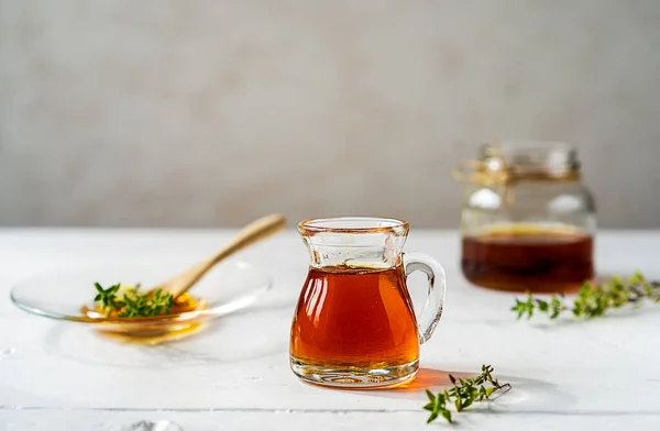 Thyme honey in small jug and jar, wooden tea spoon with honey, fresh thyme on white wooden table with grey background. Thyme honey has antiseptic and antibacterial benefits. Copy space