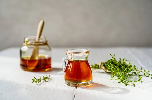 Thyme honey in small jug and jar, small thyme branch on white wooden table with grey background. Thyme honey has antiseptic and antibacterial benefits and healing effect for skin also. Copy space