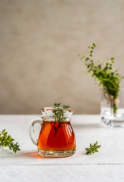 Thyme honey in small jug , thyme branch on white wooden table with grey background. Thyme honey has antiseptic and antibacterial benefits and healing effect for skin also. Vertical banner. Copy space
