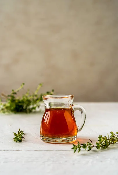 Thyme honey in small jug, fresh thyme on white wooden table with grey background. Thyme honey has antiseptic and antibacterial benefits and healing effect for skin also. Vertical banner. Copy space