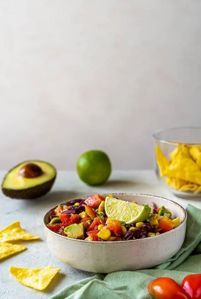 Cowboy caviar is traditional Mexican vegetable salad in bowl made with avocado, black beans, bell pepper, corn, coriander, lime juice and dip. Grey background. Vertical banner. Copy space