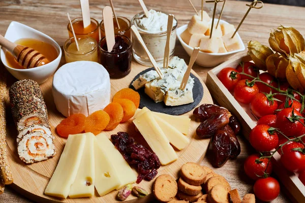 Wooden platter of soft cheeses, spreads, dried and dehydrated fruit, sweet and spicy jams with mustard, snack