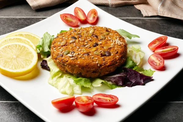 Lentils, legumes and various seeds burger, served on a salad, with cherry tomatoes and lemon slices