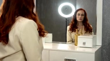 Güzel kızıl saçlı kız aynanın önünde oturuyor.