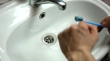 a person brushes a toothbrush in the sink under a stream of water
