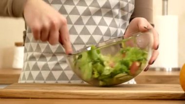 a girl stirs a salad in a transparent bowl