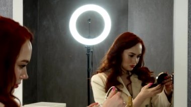 Güzel kızıl saçlı kız aynanın önünde oturuyor.