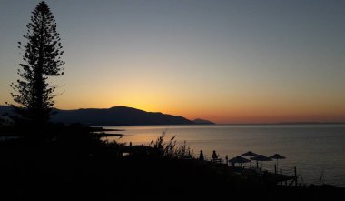 Yunanistan, Girit, Agios Nikolaos, güneş bir yaz sabahı erken saatlerde tatil beldesinin plajlarından doğuyor.