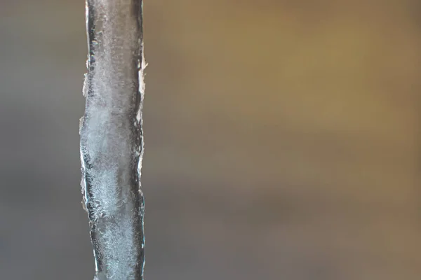 An icicle on a blurry background of blue sky and shining sun. Background with space to copy. — Stock Photo, Image