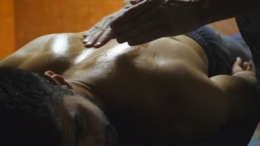 Profesyonel masajcının erkek elleri, salonda yağlı bir adama masaj yapıyor. Salondaki masaj masasında yatan kaslı sporcunun kolları. Yavaş çekim