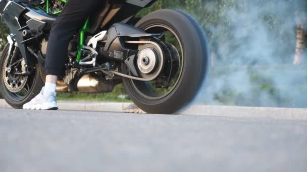 アスファルトの道路で回転し始めるスポーツバイクのホイール。大量の煙でタイヤの燃焼を行うバイカー。オートバイの車輪は動きの開始の間のルートで滑りである。スローモーション｜Close up Side view — ストック動画