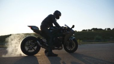 Spor motosiklet çarkı asfalt yolda dönmeye başladı. Motorcu lastik patlaması yapıyor, dumanla. Hareket başladığında motosiklet tekeri yolda kayıyor. Yavaş çekim Yan Görünümü Kapat