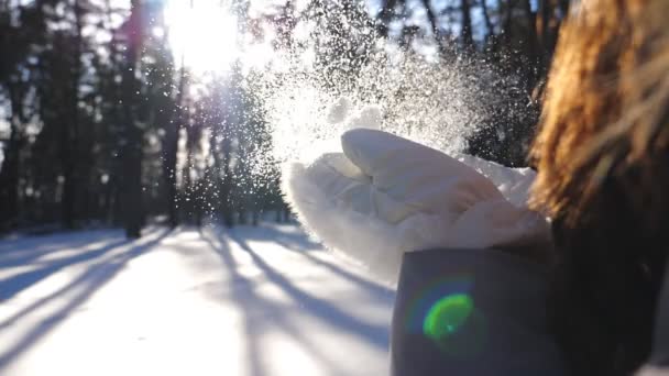 Eine unkenntliche Frau in weißen Handschuhen, die den Schnee von ihren Handflächen weht. junges Mädchen, das im Winterwald steht und an sonnigen Tagen mit Schnee spielt. verschwommener Hintergrund. Winterkonzept. Zeitlupe aus nächster Nähe — Stockvideo