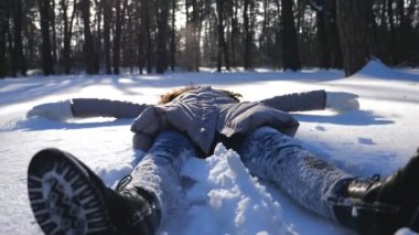 Kışın giyinmiş genç bir kız karlı çayırlarda uzanıyor ve melek yapıyor. Karda oynayan mutlu kadın kış tatilinin tadını çıkarıyor. Neşeli bayan dışarıda eğleniyor. Kış tatili kavramı. Yavaş çekim. Yakın çekim.