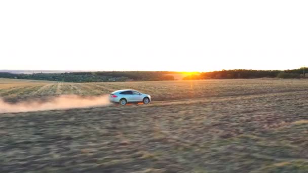 Tiro aéreo de carro eléctrico a acelerar pela rota empoeirada. Ecologia auto amigável em carga elétrica dirigindo ao longo da estrada rural com paisagem pôr do sol no fundo. Conceito de tecnologias modernas — Vídeo de Stock