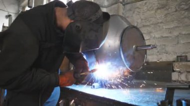 Endüstriyel üretimde koruyucu maske kaynak işçisi. Kaynakçı, metal fabrikasında iki çelik detayı arasında bağlantı kuruyor. Metal kaynak yapan adam. Yavaşça kapat.