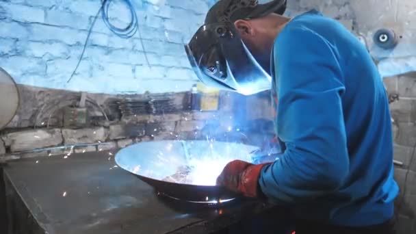 Welder welds metal detail. Worker in protective mask welding metal construction at industrial production. Manual labor with steel. Male severe job. Craftsman working at garage or metalworking factory — Stock Video