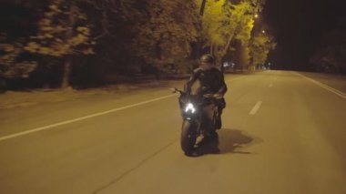 Erkek motorcu, şehir merkezinde modern motosikletiyle hareket ediyor. Gece yolunda parlak farları olan güçlü bir motorsikletle motosiklet süren bir motosikletli. Yolculuk sırasında bisiklet süren genç bir adam. Kapat.