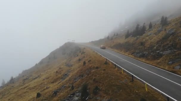 Foto aérea de coche naranja a caballo a través de la carretera de montaña en otoño. Conducción automática en la ruta de la niebla. SUV moviéndose a través de paisaje escénico camino en la hermosa temporada. Concepto de viajar. Vista superior — Vídeos de Stock